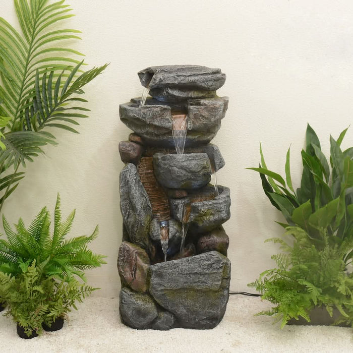 A 5-tier rock-design water fountain near plants.