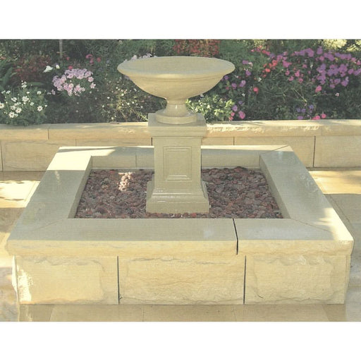 A square concrete pond with a fountain in the middle.