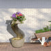Modern spiral water fountain with LED lighting and a vibrant flower arrangement on top, set against a white brick wall with garden tools nearby.