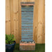 Tall slate water feature with horizontal ridges and copper trim, placed in a garden setting with pebbles at the base.