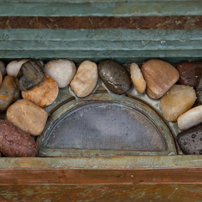 Close-up of fountain base with mesh-covered water inlet surrounded by smooth decorative pebbles.