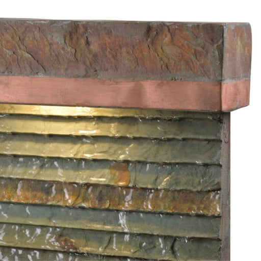 Close-up of textured slate fountain with copper trim and water flowing down stone surface.