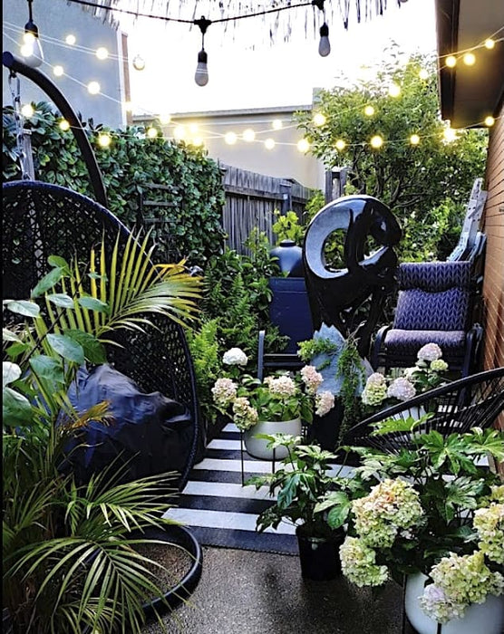 Cozy garden with an angel fountain, vibrant greenery, hydrangeas, and warm string lights for an inviting ambiance.