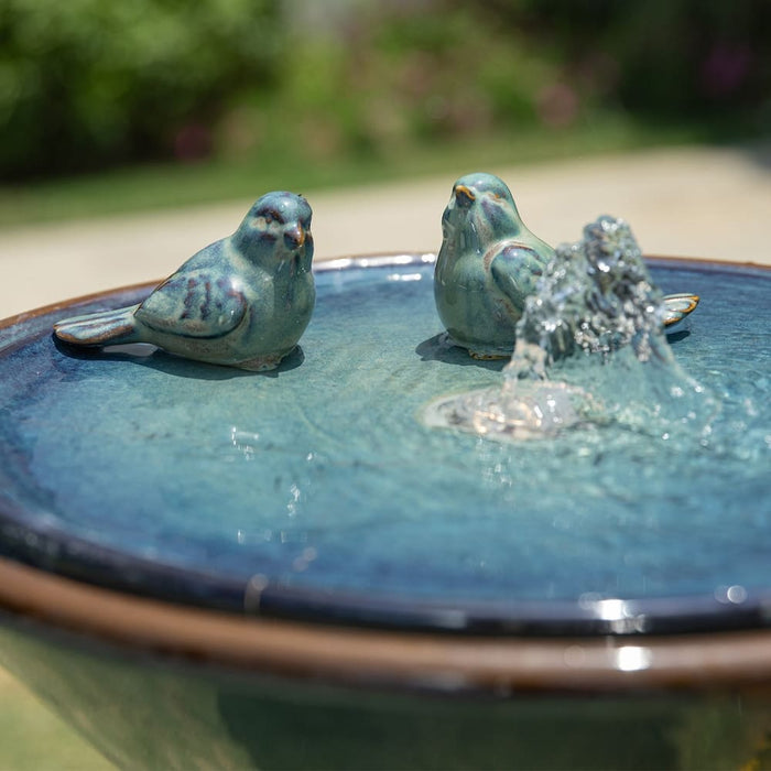 Two birds on the basin of a birdbath fountain.