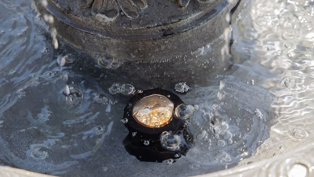 Close-up of an LED light submerged in a water fountain, surrounded by rippling water and small air bubbles.
