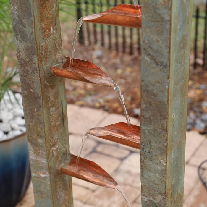 Outdoor slate water fountain close-up with cascading water over copper spouts.