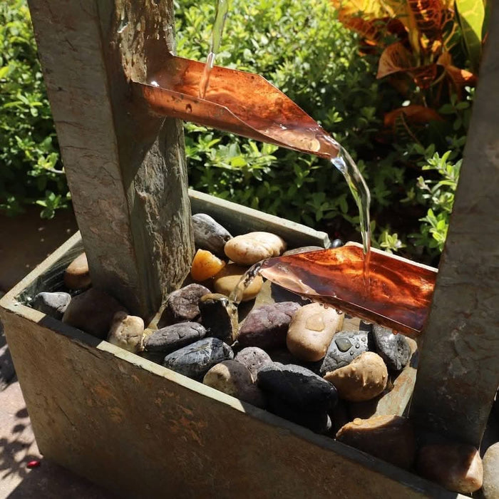 Close-up of copper spouts on a slate water fountain with water flowing over smooth river stones.