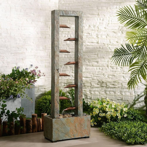 Slate water fountain with copper spouts in a stone base, surrounded by garden plants.