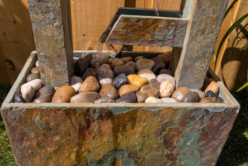 Close-up of slate water fountain base with water flowing onto smooth decorative river stones.
