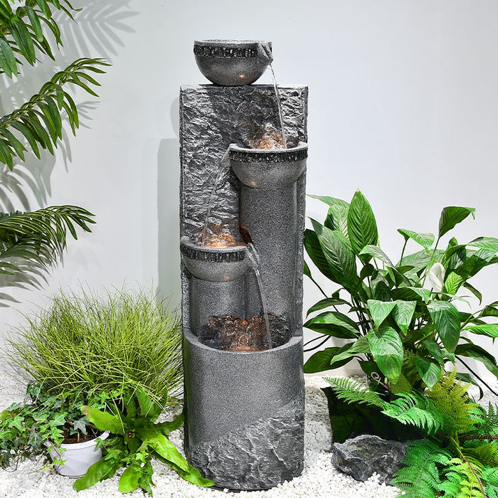 A 4-tier stone fountain near plants.